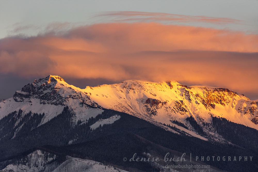 The last light of day strikes a mountain ridge with warm light, coloring the clouds pink.